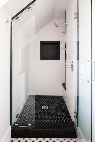 Small attic shower with black hexagon floor tiles, glass door, and built-in niche.