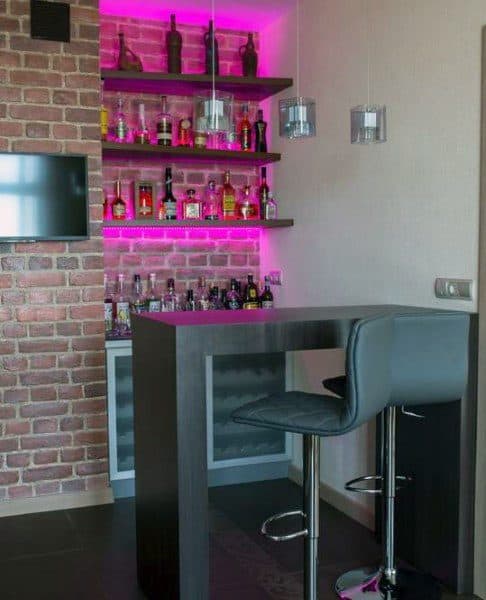 Modern mini bar with pink LED lighting, brick wall, floating shelves, and bar seating.