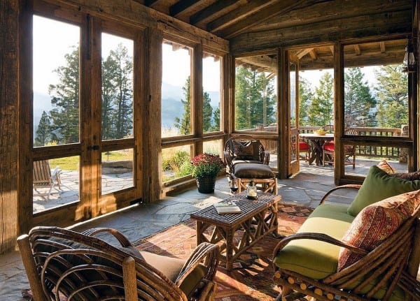 A rustic sunroom with wooden beams, wicker furniture, a stone floor, and cozy green and orange cushions.