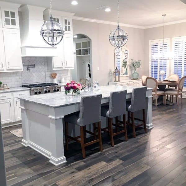 Elegant kitchen with dark wood flooring, white cabinetry, marble countertops, and modern pendant lighting