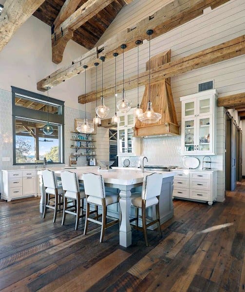 This kitchen features stunning island lighting, with glass pendant lights that complement the rustic wooden beams and spacious layout