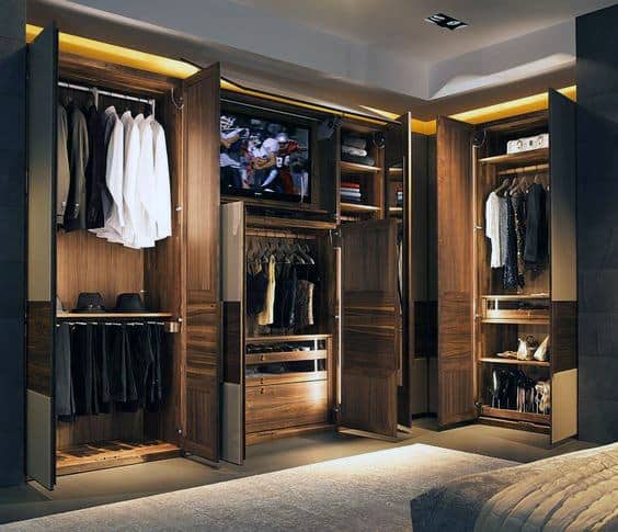 Open wooden wardrobe with clothes, shoes, and a TV inside, illuminated by warm lights