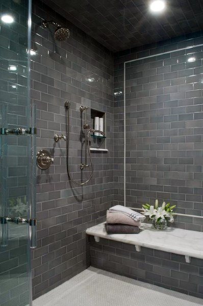 Dark grey subway-tiled shower with marble bench, glass door, and recessed shelf.