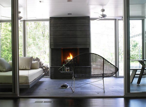 The sunroom showcases a modern fireplace, glass walls, and sleek black wire seating with neutral furnishings.