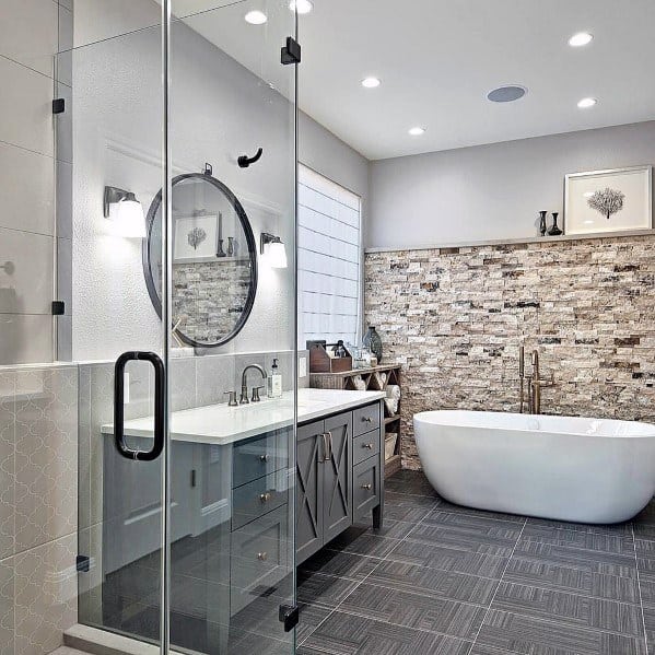 Country-style bathroom with freestanding white tub, stone accent wall, and glass shower enclosure.