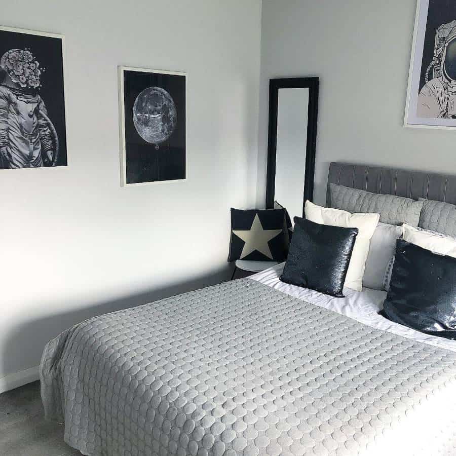 Modern bedroom with grey quilted bedding, space-themed wall art, and black accent pillows.