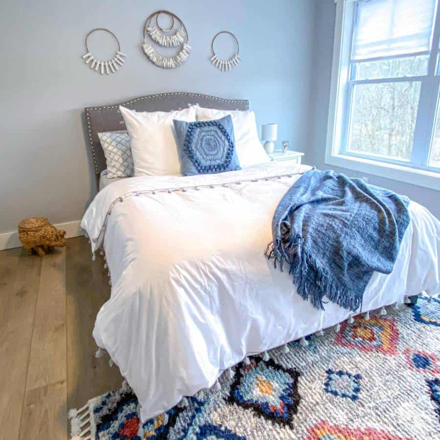 Bright boho bedroom with white bedding, blue accents, and decorative wall hangings