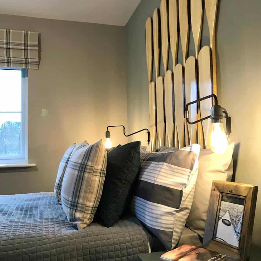 Cozy bed with multiple plaid and striped pillows, unique paddle headboard, and industrial wall lights.