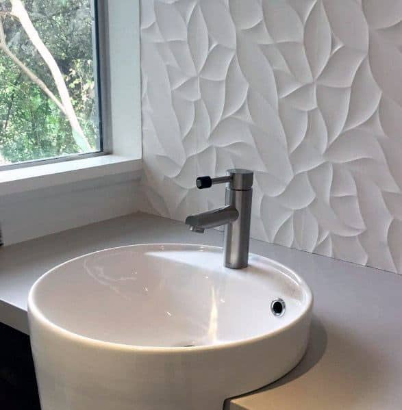 Round bathroom sink with textured leaf-patterned white wall tiles.