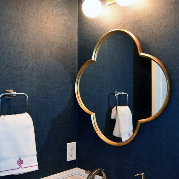 Bathroom with navy textured wallpaper and gold quatrefoil mirror.