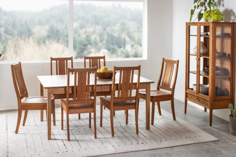 Wooden dining set with six chairs, table, display cabinet, and scenic window view.