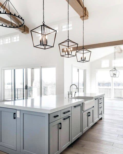 Three geometric chandeliers illuminate a sleek gray kitchen island, creating an elegant and airy modern space