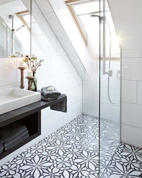 Attic bathroom with floral patterned floor tiles, glass shower, and sloped window ceiling.