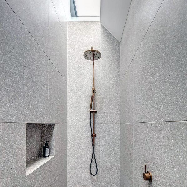 Shower with grey terrazzo tiles, copper rain showerhead, and built-in wall shelf for toiletries.