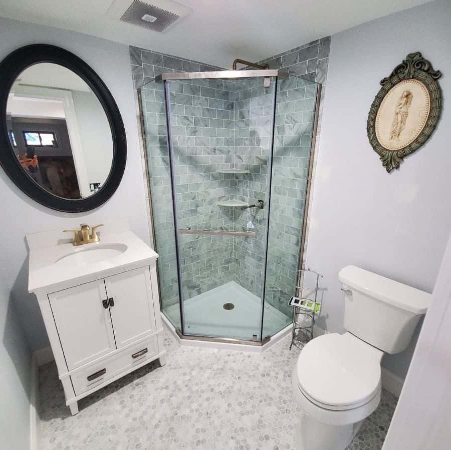 White bathroom with green tiled corner shower, round mirror, and white vanity.