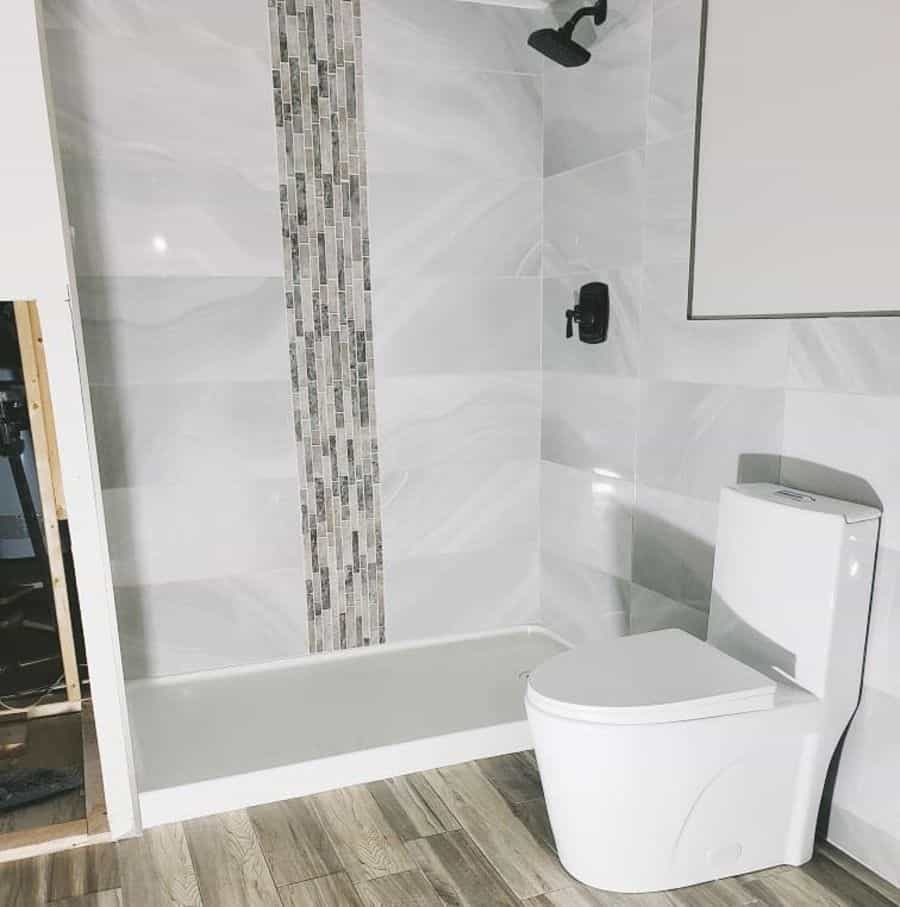 Contemporary bathroom with vertical accent tiles in shower, modern toilet, and wood-look flooring.