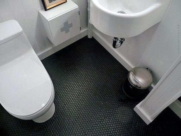 White toilet with black hexagonal tiled floor and small wall-mounted sink.