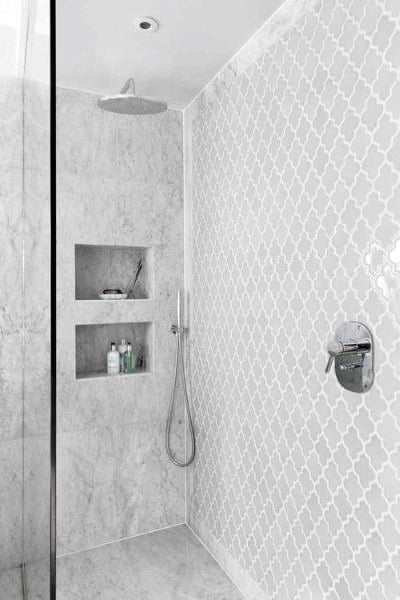 Walk-in shower with white geometric patterned tiles and built-in wall shelves for toiletries.