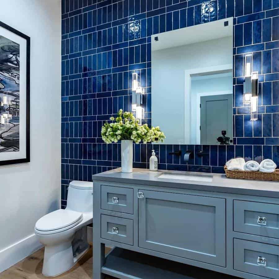 Modern bathroom with blue tile accent wall, large mirror, gray vanity, and flowers in a vase next to towels in a basket