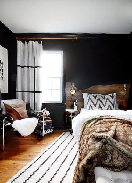 Cozy bedroom with black walls, wooden headboard, fur blanket, and striped rug.