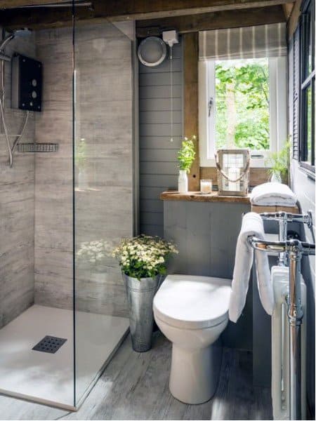 Rustic bathroom with shower, toilet, plants, and window, featuring wooden and gray decor