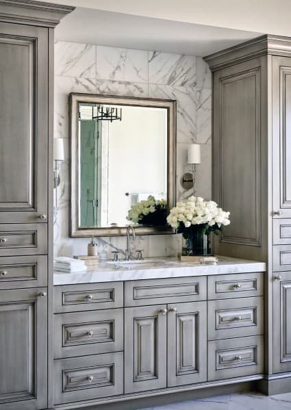 Traditional bathroom vanity with grey cabinets, marble backsplash, and a framed mirror.