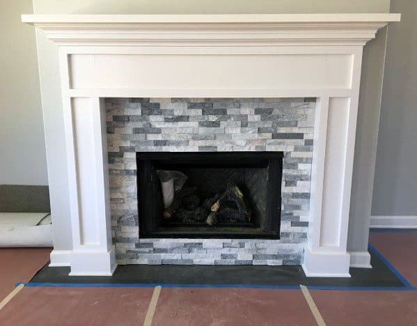 A classic fireplace with grey and white stacked stone tiles framed by an elegant white mantel.