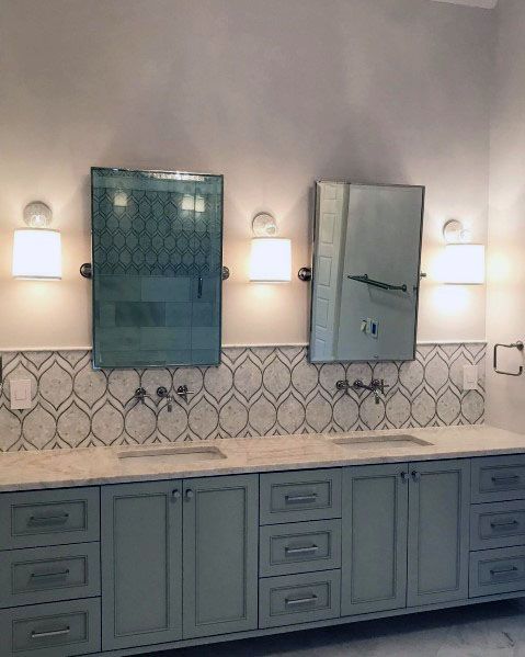 Patterned tile backsplash with double vanity, light blue cabinetry, and wall-mounted mirrors.