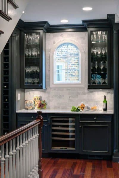 Traditional mini bar with dark cabinets, glass displays, marble backsplash, and arched window.