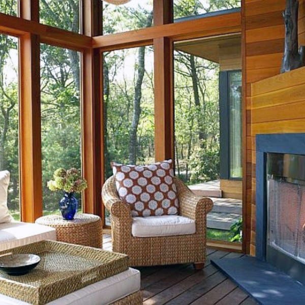 Sunroom with wood walls, wicker furniture, large windows, and cozy fireplace corner.