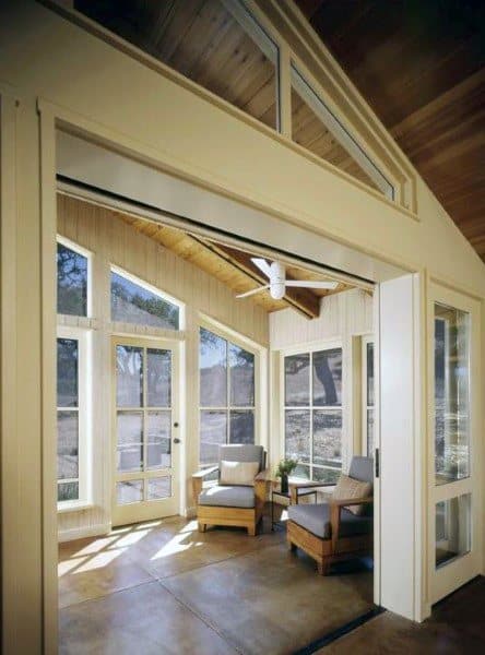 Bright sunroom with vaulted wood ceiling, large windows, and cozy armchairs for seating.