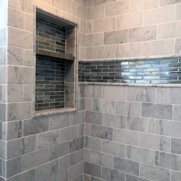 Marble bathroom with recessed shelves and green glass tile accents.