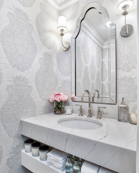 Elegant bathroom with marble vanity, ornate mirror, and gray patterned wallpaper.