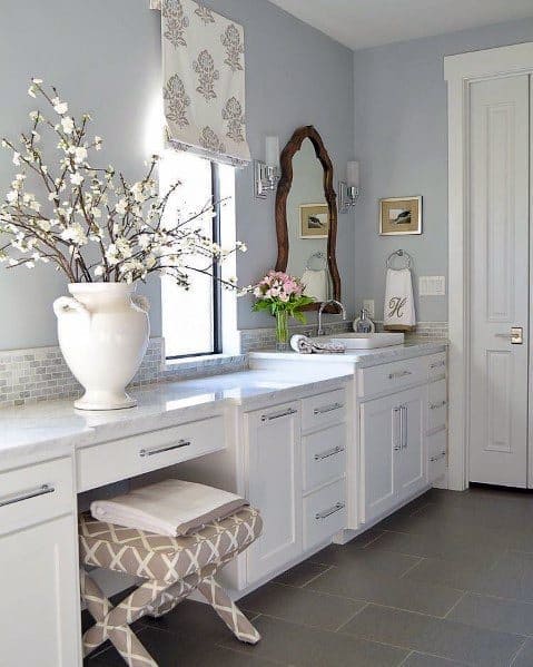 Traditional white bathroom with marble countertop, decorative mirror, and floral accents.