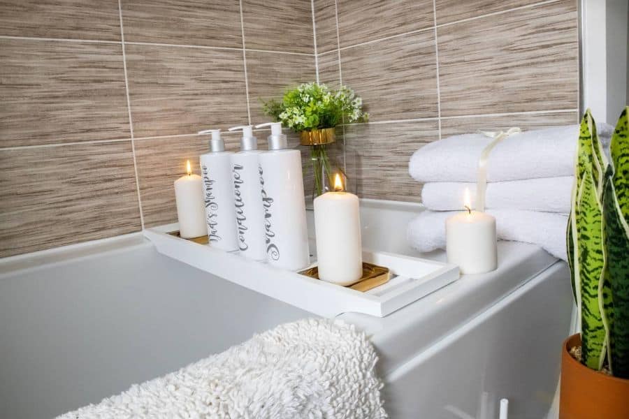 Bathtub tray with candles, shampoo bottles, towels, and a small plant for a spa-like feel.