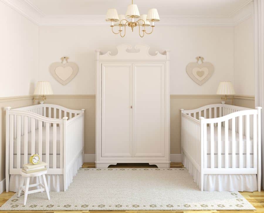 Classic baby room for twins with two white cribs, a central wardrobe, and heart-shaped wall decor.