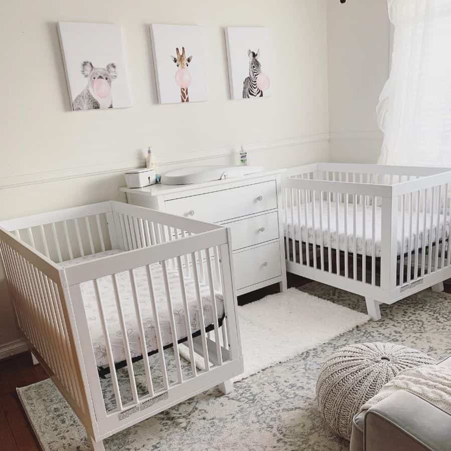 Baby room for twins with white cribs, playful animal prints, and soft neutral decor with a changing table in the middle.