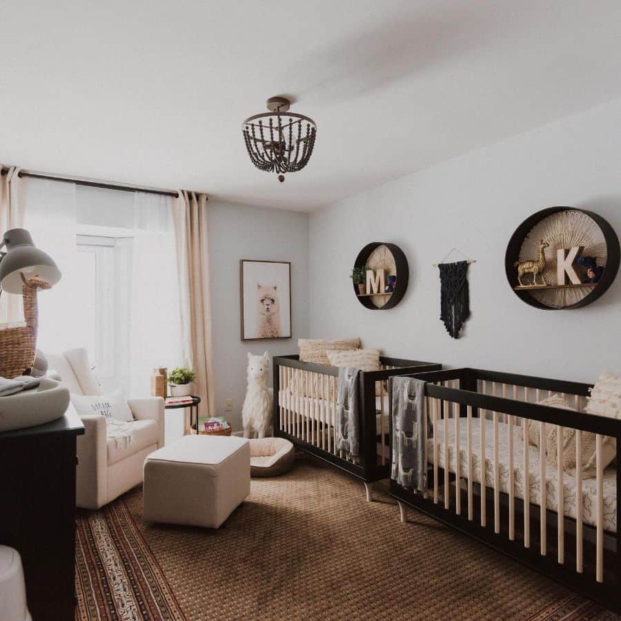 Twin baby room with dark cribs, personalized decor, alpaca artwork, and cozy boho accents.