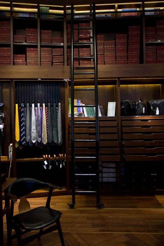 A luxurious walk-in closet with ties, shirts, a ladder, and shelves filled with boxes and books