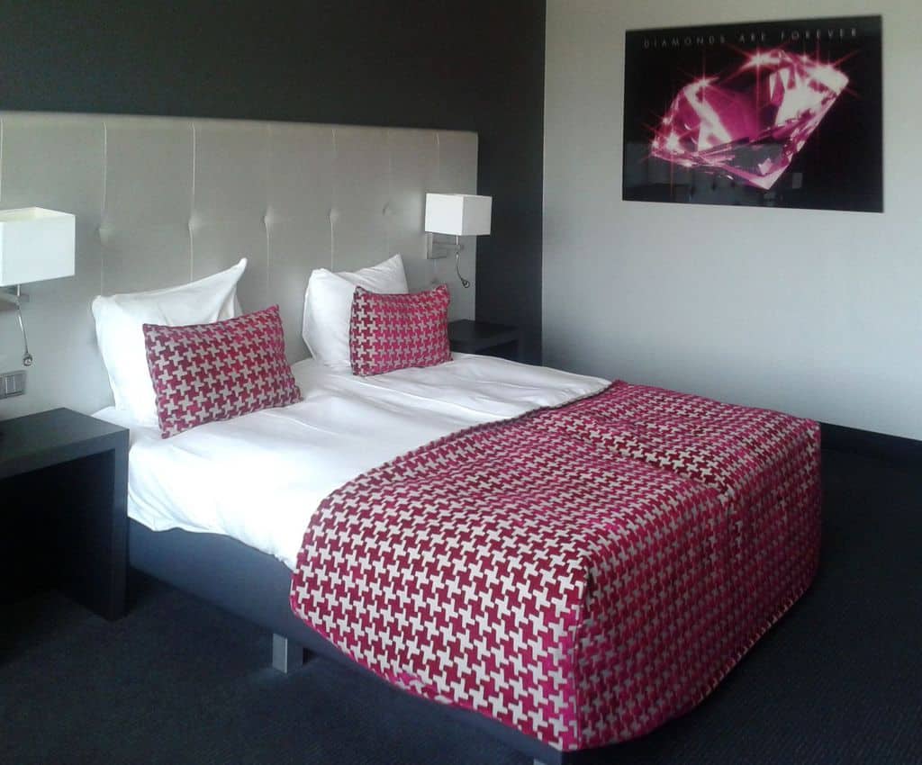 Two-tone bedroom with red patterned bedding, tufted headboard, and diamond-themed wall art.