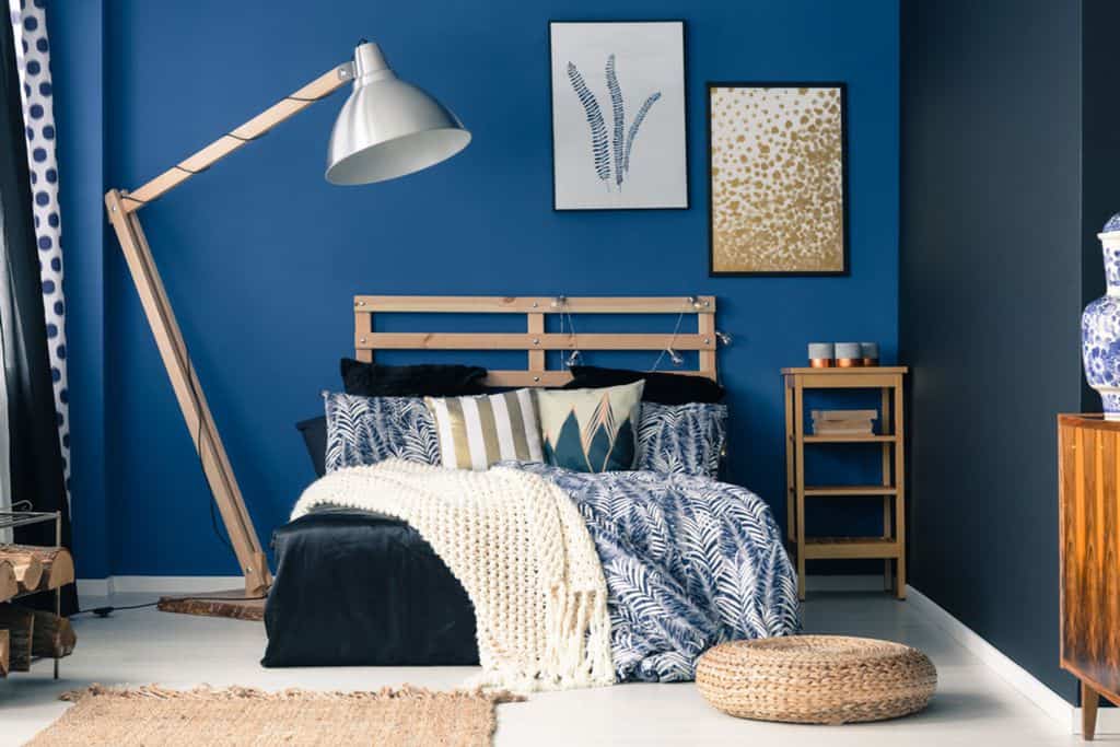 Two-tone blue bedroom with a wooden bed, oversized lamp, and nature-inspired decor.