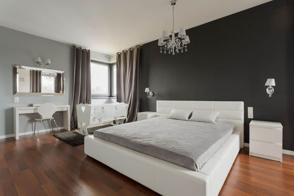 Two-tone gray bedroom with king-size bed, white furniture, crib, and chandelier lighting.