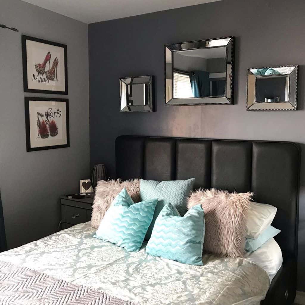 Modern bedroom with mirrored wall decor, black leather headboard, and pastel throw pillows.