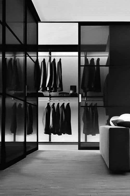 Minimalist closet with black coats and jackets hanging neatly, reflecting in the glass doors