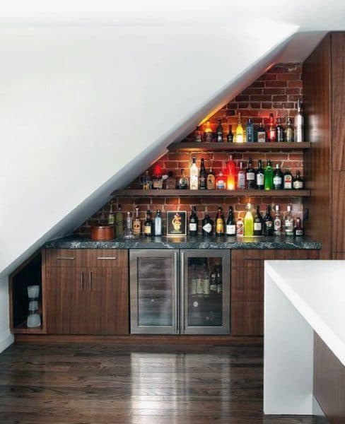 Under-stair mini bar with brick backsplash, wood cabinets, marble countertop, and beverage fridge.