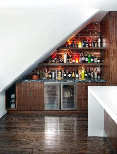 Under-stair mini bar with brick backsplash, wood cabinets, marble countertop, and beverage fridge.