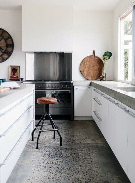 Modern kitchen with unfinished concrete flooring, white cabinetry, and minimalist design featuring a wooden stool