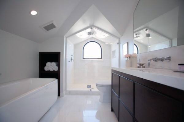 Modern bathroom with a bathtub, shower, and vanity under a vaulted ceiling and arched window