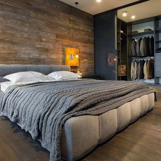 Cozy bedroom with a gray upholstered bed, textured wall, warm lighting, and an open closet with hanging clothes