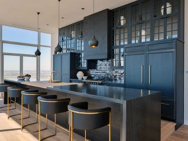 Modern black kitchen with glass-front cabinets, large island, gold-accented bar stools, and pendant lights.